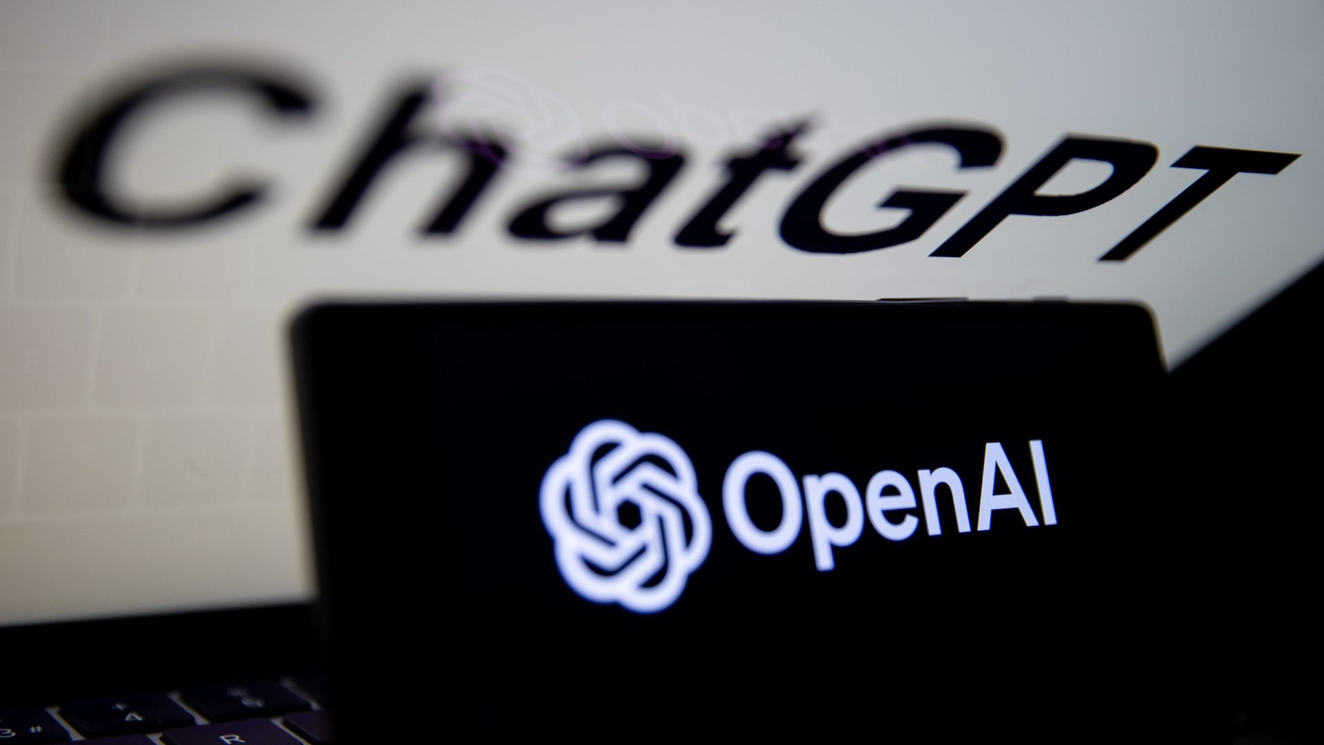 OpenAI logo is being displayed on a mobile phone screen in front of computer screen with the logo of ChatGPT